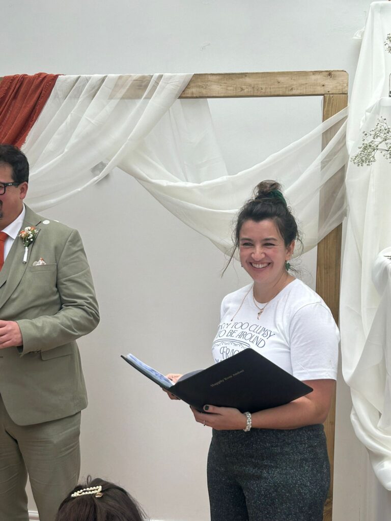 An image of a celebrant smiling, holding a book whilst delivering a ceremony. 