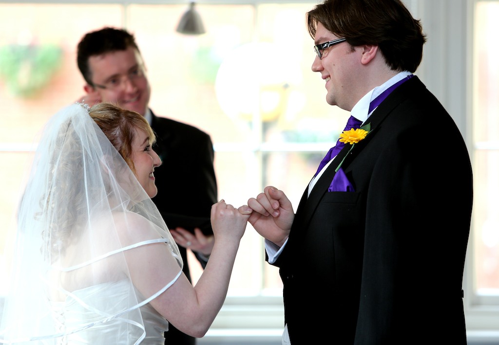 Andy and Lea shaking pinkies while Ewan conducts ceremony