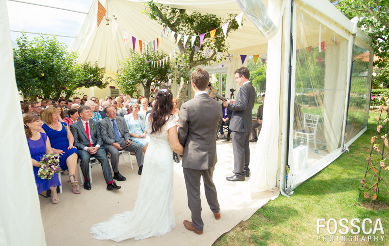 Bride and groom stand in front of their guests in a marquee filled with trees