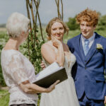 A bride and groom looking at their humanist wedding celebrant in an outdoor humanist wedding in Wiltshire.
