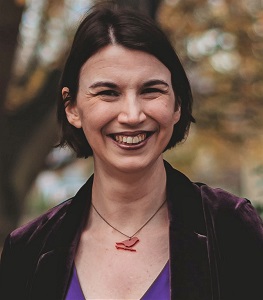 Picture of Kathryn - face on, smiling, short dark harir, dark purple velvet jacket and a red bird necklace