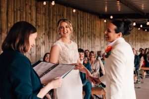 Two women smile as they look at their wedding celebrant, while saying their vows.