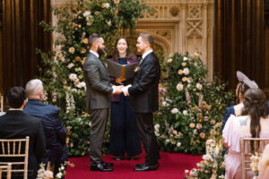 Two men make their wedding vows in a grand hall decorated with a dramatic floral installation.