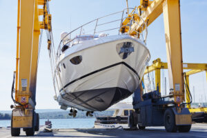 Sleek speed boat being carried in a wheeled, yellow crawler-crane