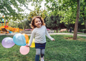 Child smiling running with coloured balloons in the garden